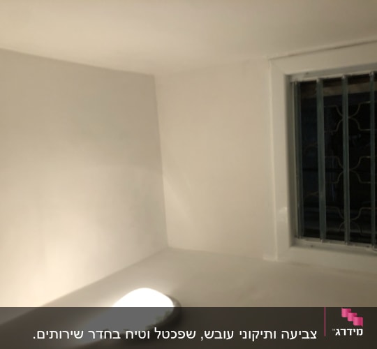 קיר צבוע בלבן עם חלון וסורגי מתכת